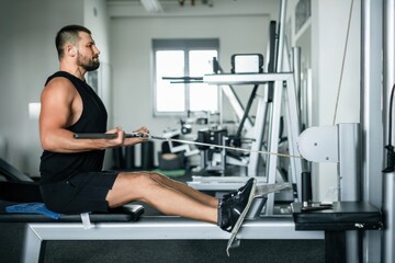 Athletic man training on a cable row machine in a modern gym © Cavan