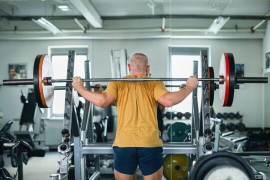 Muscular man lifting a barbell for squats in the gym