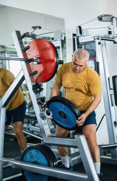Muscular man adjusting weight plates on a squat machine in the gym