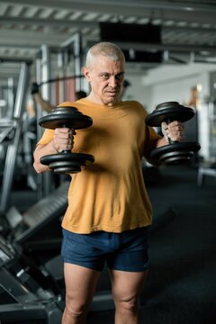 Determined middle-aged man lifting heavy dumbbells in the gym