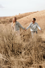 A couple walks hand in hand, exploring a sunlit, hillside together