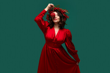 Playful woman in red dress holding Christmas ornament above her face