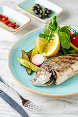 Grilled sea bream with vegetables and greens on white background