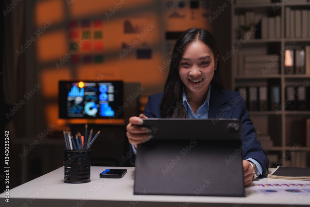 Poster smiling businesswoman working late in an office, showcasing a tablet while analyzing data on a compu