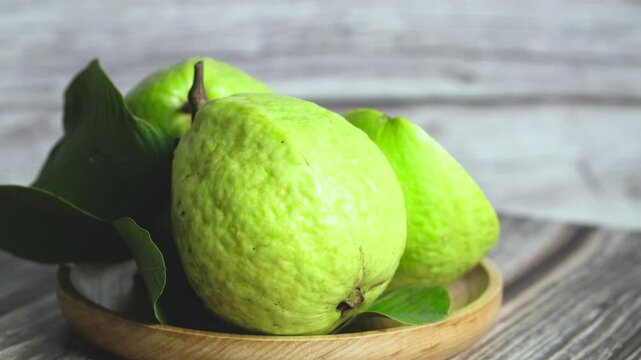 Rotating plate of guavas with a half-cut fruit and two whole guavas with leaves &ndash; side view mid-range shot