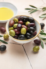 Bowl of assorted olives with olive oil and olive branches on tiled surface