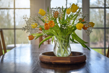 Bouquet of yellow and orange tulip flowers on a wooden table in front of large windows in the living room, spring and Easter decoration, copy space, selected focus
