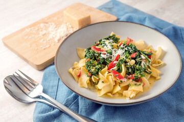 Tagliatelle pasta with spinach and red bell pepper sauce, garnished with parmesan cheese in a gray plate on a blue napkin, cooking vegetarian, selected focus