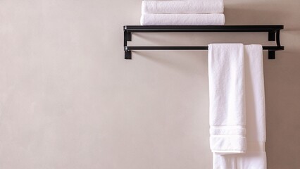 Obraz premium Bathroom wall-mounted black metal towel rack with white towels, minimalist luxury interior with beige background and copy space.