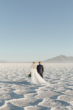 Bride and groom standing in a  vast salt flat looking at mountains