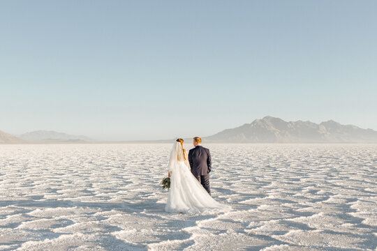 Landscape scene of loving bride and groom on a salt flat holding hands