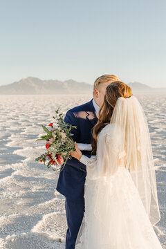 Bride and groom embracing on a salt flat with a mountain backdrop.
