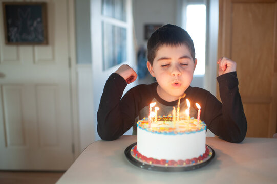 Young boy blows out candles on his birthday cake at home in kitchen