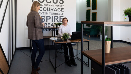 Two professionals engage in discussion in a modern office during the daytime with motivational words prominently displayed
