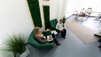 Fototapeta premium Two professionals collaborate in a modern office lounge with greenery and casual seating during a productive work session