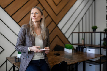 Business professional sitting at a modern workspace, contemplating while holding a smartphone...