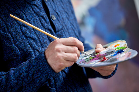 the artist holds a palette with paints and a brush and is going to paint on canvas