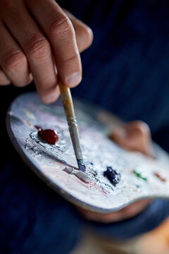 the artist holds a palette with paints and a brush and is going to paint on canvas