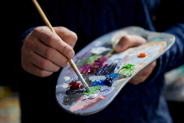the artist holds a palette with paints and a brush and is going to paint on canvas