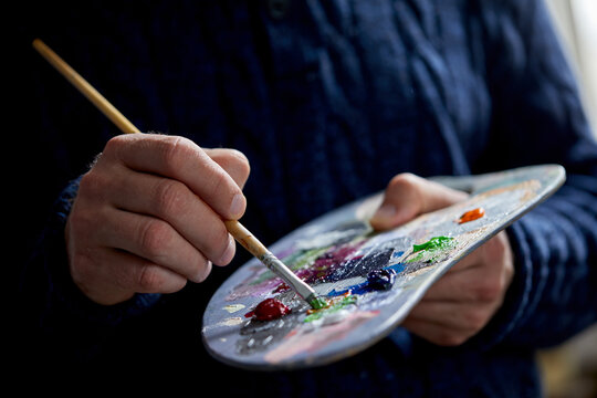 the artist holds a palette with paints and a brush and is going to paint on canvas