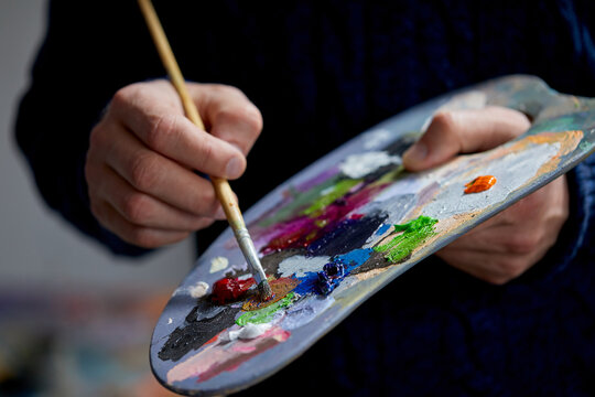 the artist holds a palette with paints and a brush and is going to paint on canvas