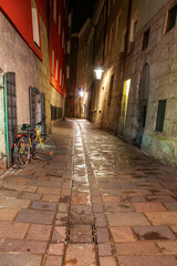 Fototapeta premium Quaint cobblestone alley in Innsbruck's historic center illuminated by warm streetlights. A colorful bicycle adds character to the scene, highlighting the city's blend of old and new