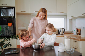 Sisters working together to knead dough while mother observes fostering teamwork and sibling...