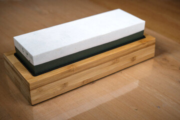 A dual-grit whetstone with a white and green sharpening surface on a bamboo base, designed for honing knives and tools with precision and stability.