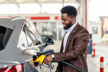 Smiling interracial man filling up car tank at gas station.