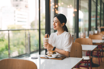 Happy asian woman healthy eating breakfast sandwich at cafe sitting near window indoors on day
