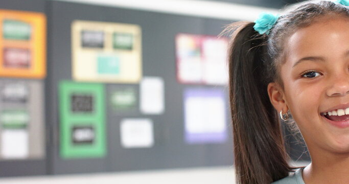 Smiling girl in school classroom with colorful bulletin board in background, copy space - Powered by Adobe