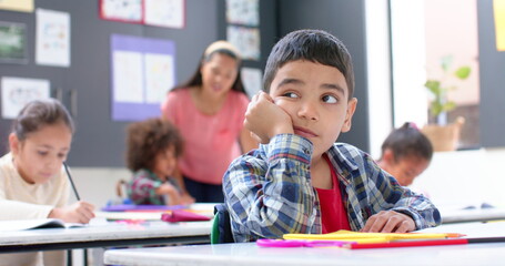 In school, boy daydreaming at desk while classmates and teacher working