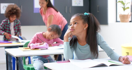 In school, girl daydreaming at desk while classmates and teacher working