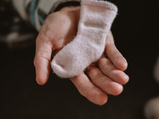 Gentle hand holds a tiny pink newborn sock, symbolizing care and warmth for a new life. Close-up...