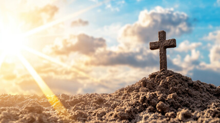 A cross stands tall on a mound of sand illuminated by warm sunset light, with clouds softly glowing