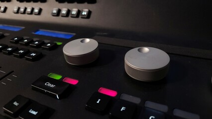 Close-up of a professional lighting control panel with illuminated buttons, rotary dials, and a...