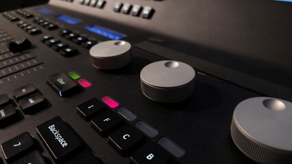 Close-up of a professional lighting control panel with illuminated buttons, rotary dials, and a...