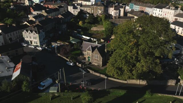 Clones Town, County Monaghan, Ireland, September 2022. Drone pulls backwards from Cassandra Hand Heritage Centre, revealing the Round Tower and view of the historic town, architecture, and landscape.