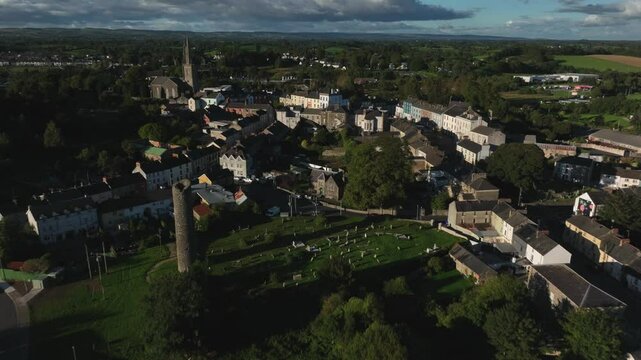 Clones Town, County Monaghan, Ireland, September 2022. Drone pulls backwards from the medieval round tower and Cassandra Hand Heritage Centre, revealing the cemetery, and historic townscape.