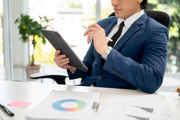 Close up of businessman or male office worker looking at tablet in right hand and holding a stylus...