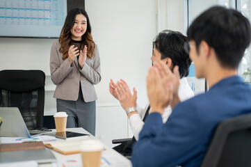 Businesswoman or female office worker is smiling while standing and clapping hands with coworkers.