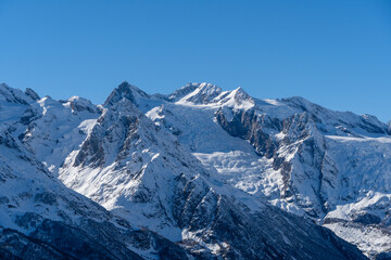 Obraz premium Snow-capped peaks with majestic blue slopes rise above jagged slopes of North Caucasus Range. Mountain tops are covered with eternal glaciers. Dombay. Karachay-Cherkessia.