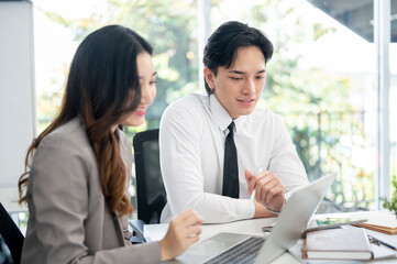Female office worker and her male coworker is smiling while talking together at the working desk.