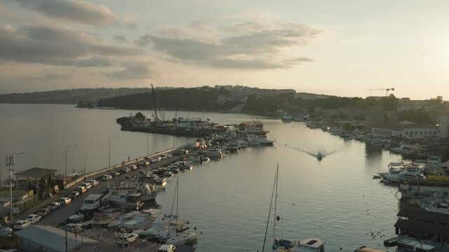 A bustling Turkish marina with yachts glows at sunset, reflecting a trend of luxury coastal tourism and serene yachting escapes against a hilly backdrop. Sinop, Turkey
