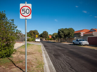 A quiet suburban street in Melbourne, Australia with a 50 km/h speed limit sign on roadside. A...