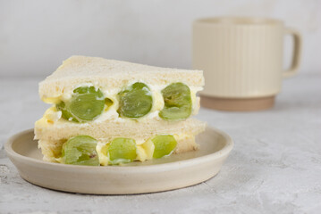 Half sandwiches bread stuffed with mascarpone cream cheese, grape and cup of tea. Homemade Korean dessert.