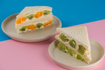 Homemade Korean style bread sandwiches with kiwi, orange, grape and cream cheese on a blue and pink background.