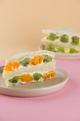 Homemade Korean bread sandwiches with kiwi, orange, grape and cream cheese on a beige and pink background. Asian street dessert. Vertical orientation.