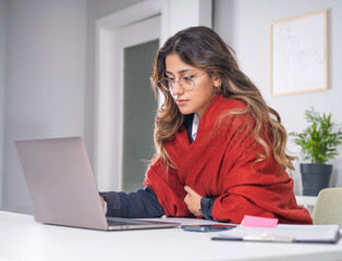 Businesswoman feeling unwell after catching cold, side view profile image of young caucasian brunette 20s businesswoman feeling unwell after catching cold in office using laptop wrapped in scarf.