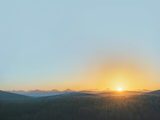 Fototapeta premium The most magnificent peaceful sunset sky with warm sun rising gradually transitioning to a light blue sky. Vast serene landscape with mountain range in the horizon. Trees and forests in a distant shot